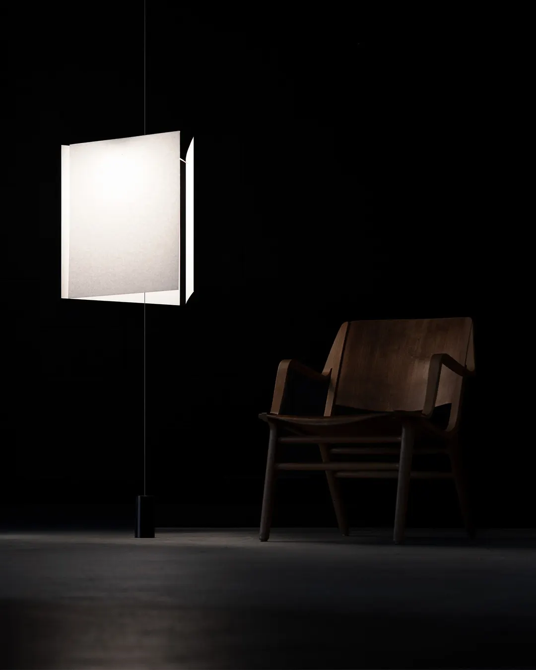 Lampada miimale sospesa con, sullo sfondo scuro, una sedia in legno